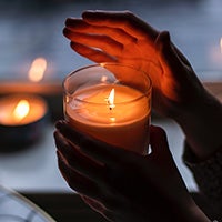 A hand protects a burning candle.